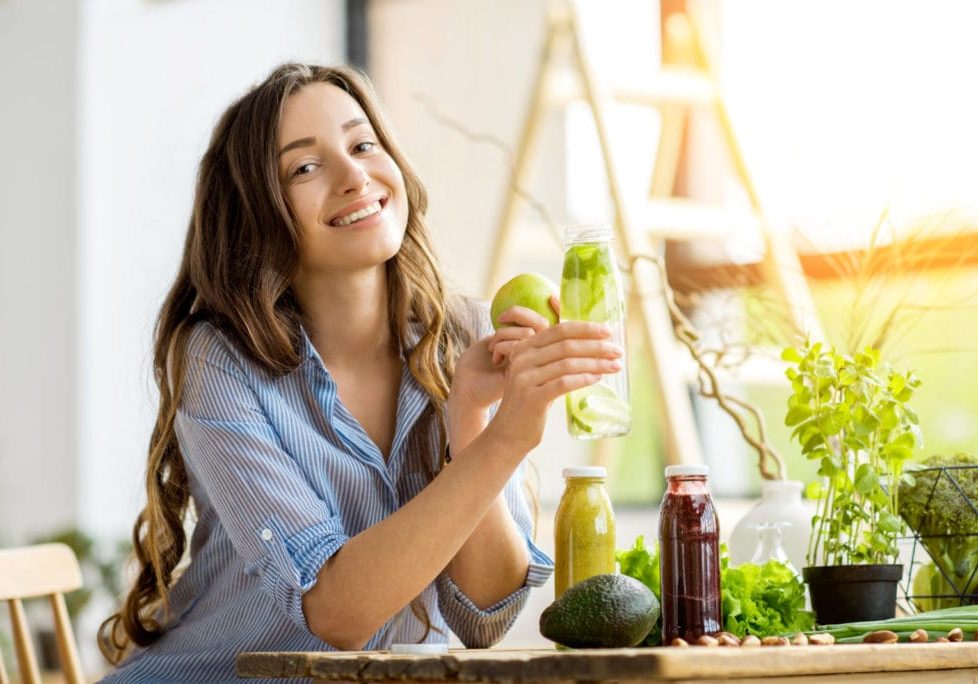 Beautiful happy woman sitting with drinks and healthy green food at home. Vegan meal and detox concept