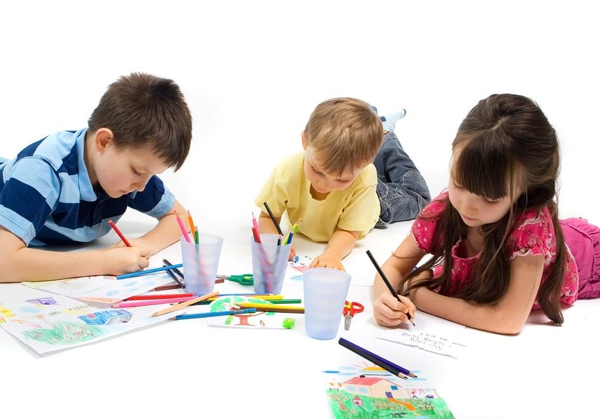 Three children brothers and their sister laying on the floor quietly entertaining themselves by drawing and coloring their favorite picture.