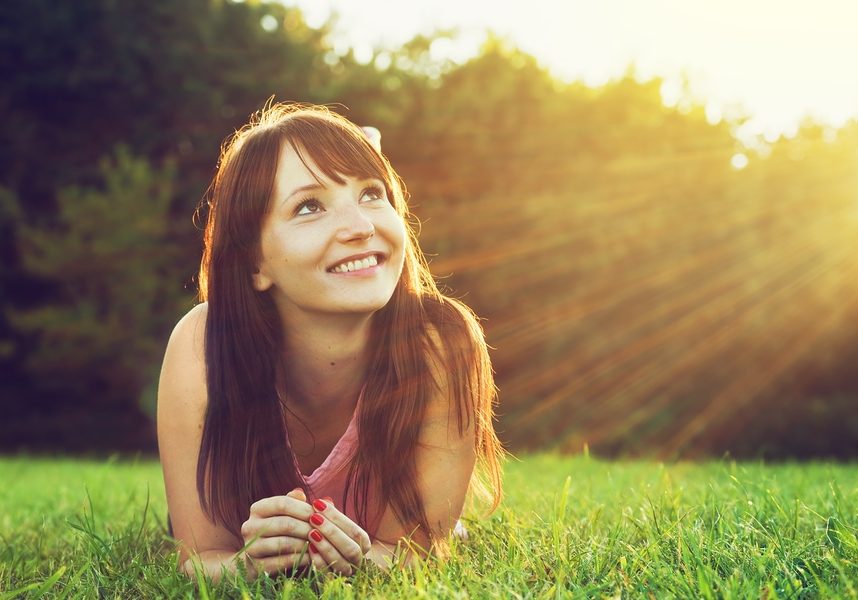 Young pretty woman lying on the grass at summer sunset. Natural happiness, fun and harmony.