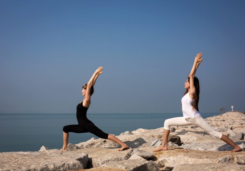 Beautiful young woman practicing yoga on the beach on the rocks. Virabhadrasana